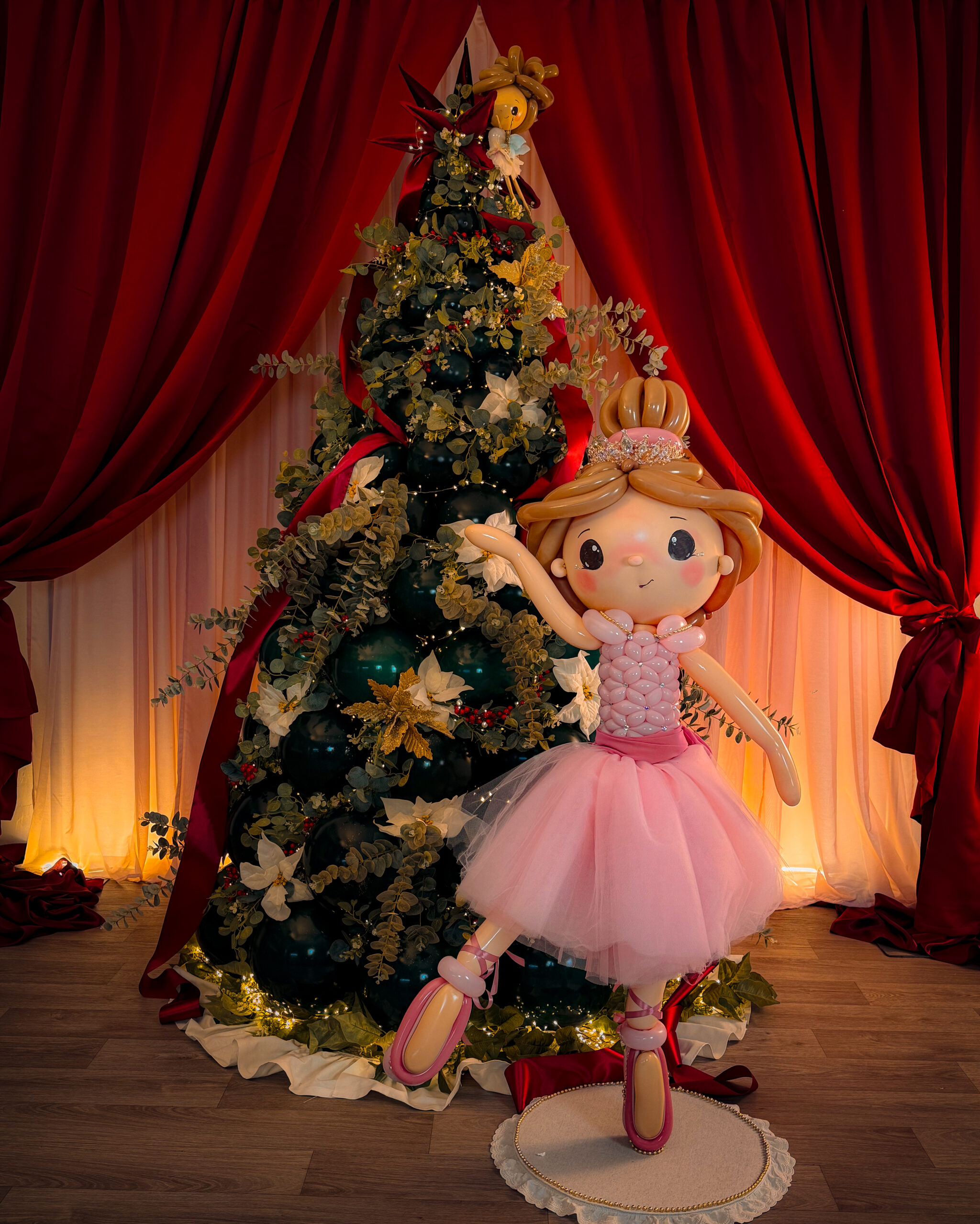 Bailarina creada con globos ante un árbol de Navidad y cortinas burdeos