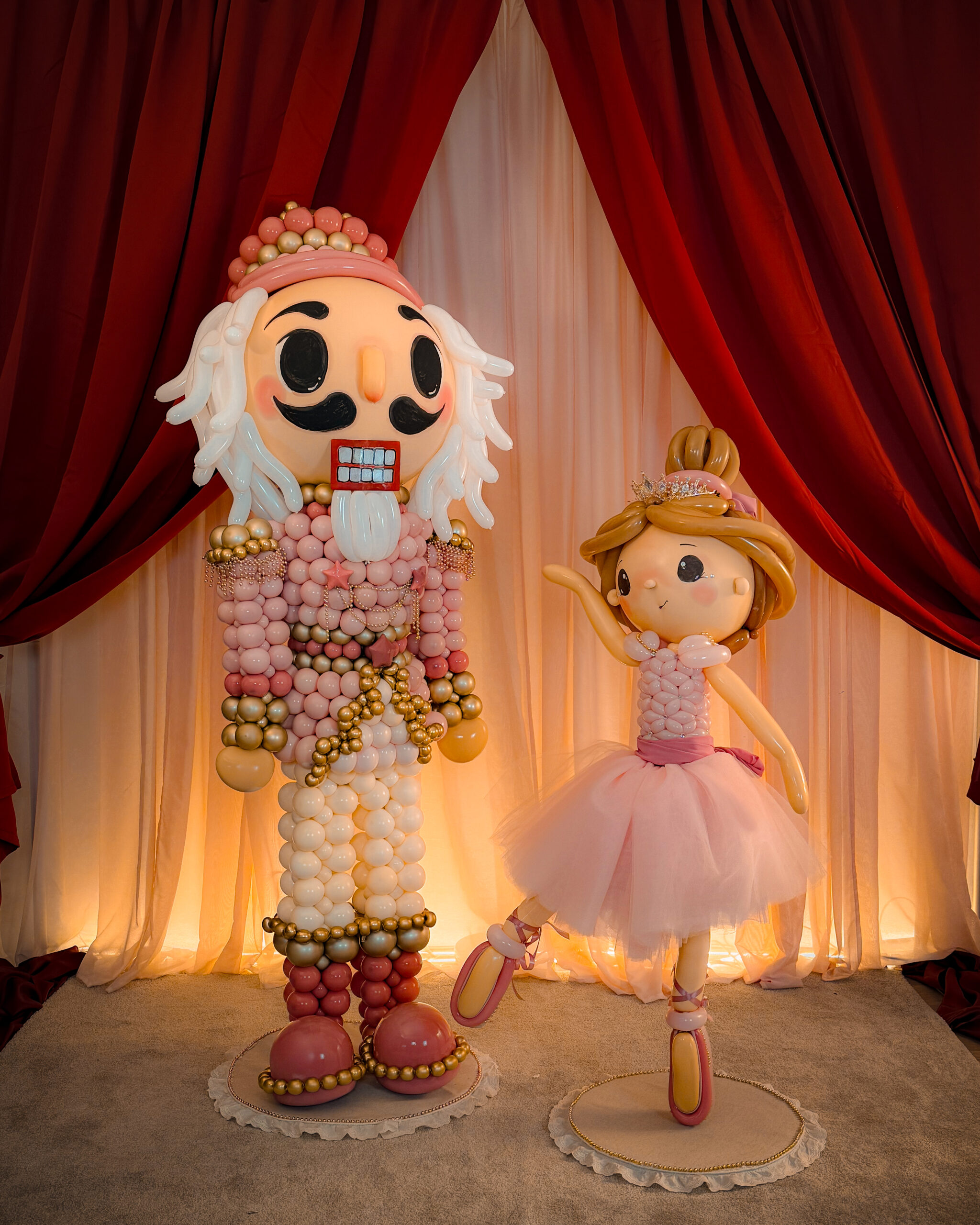 Cascanueces rosa y bailarina de globos bajo cortinas burdeos iluminadas